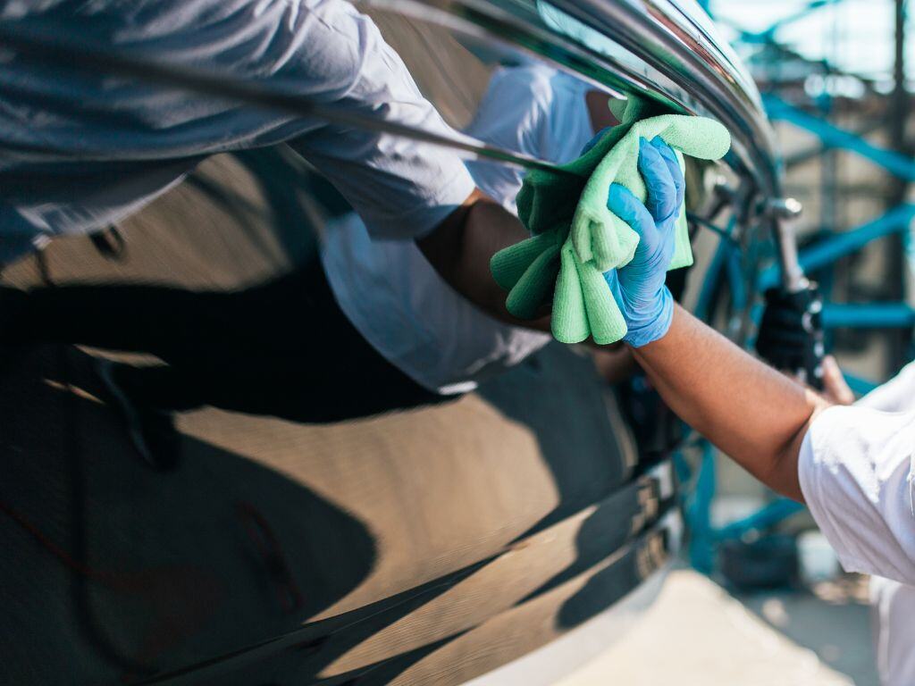 Boat detailing professional wiping down a polished boat hull with a microfiber cloth, ensuring a streak-free finish at a marina.