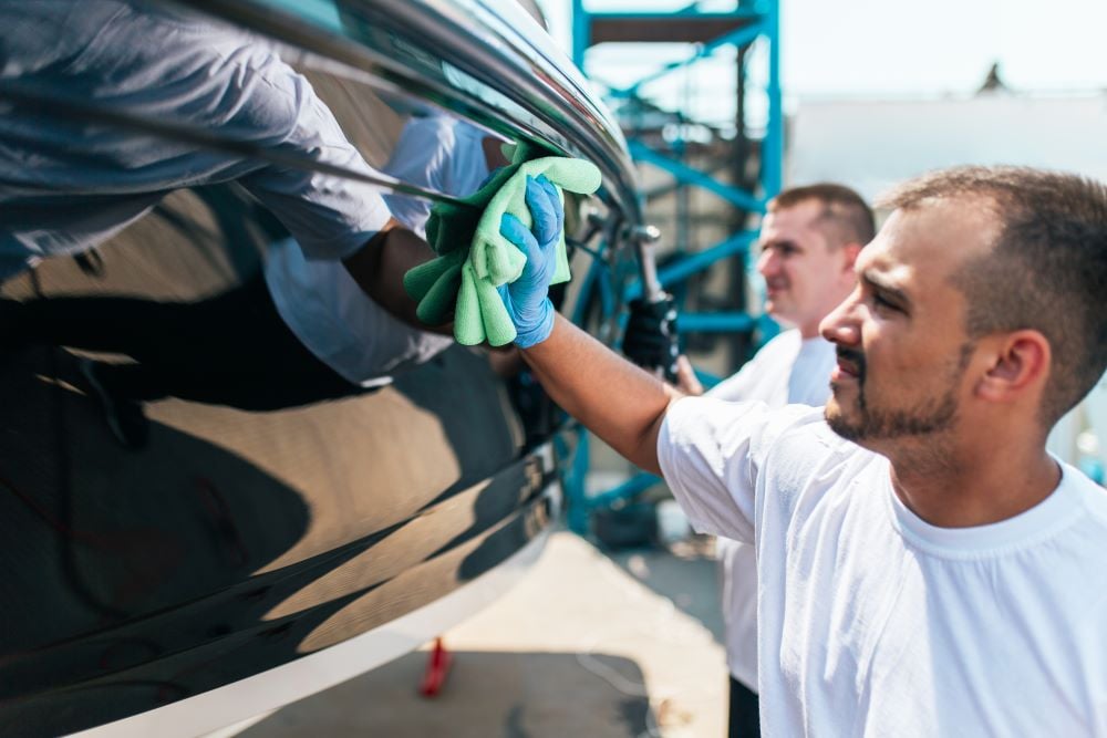 Boat detailing professionals wiping down a polished boat exterior with microfiber cloths, ensuring a streak-free finish at a marina.